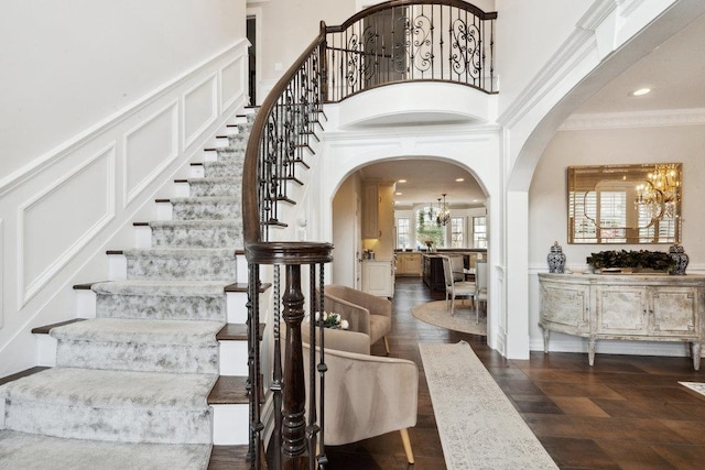 staircase featuring wood finished floors, an inviting chandelier, arched walkways, crown molding, and a decorative wall