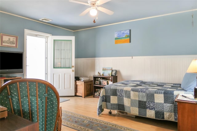 bedroom with visible vents, ornamental molding, a ceiling fan, wood finished floors, and wainscoting