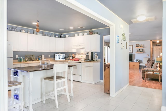 kitchen with white cabinetry, stainless steel microwave, a kitchen breakfast bar, and electric stove