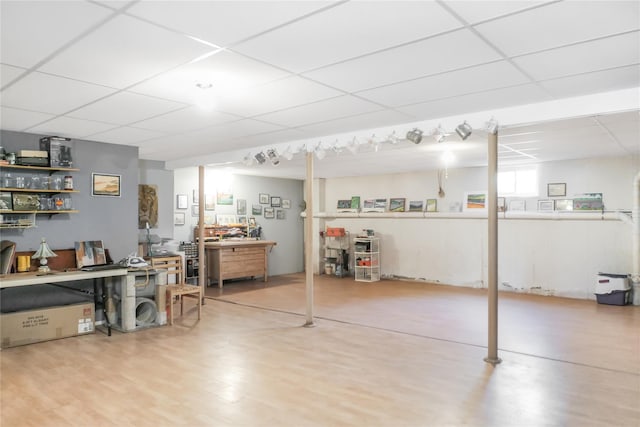 basement with a drop ceiling, a workshop area, and wood finished floors