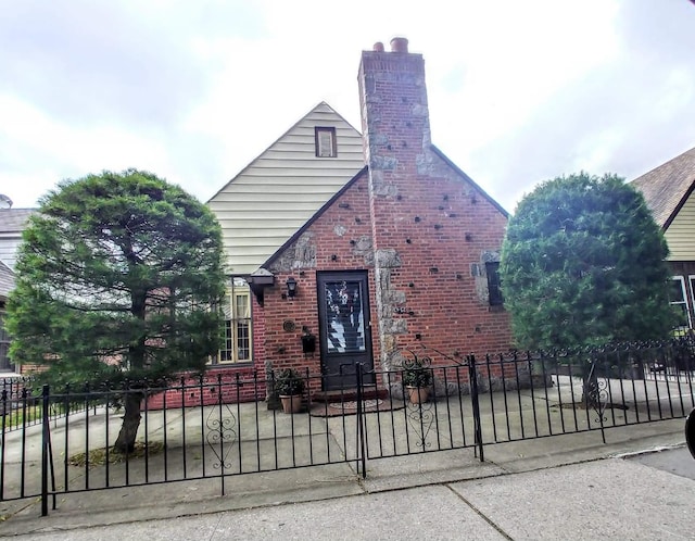 view of front facade featuring brick siding, a chimney, and a fenced front yard