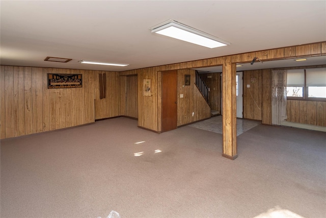 basement featuring light carpet, wood walls, and stairs