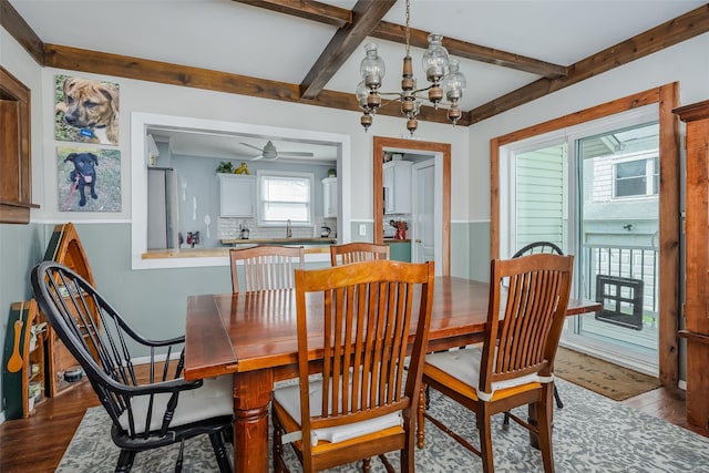 dining room with beamed ceiling, ceiling fan with notable chandelier, and dark wood-type flooring