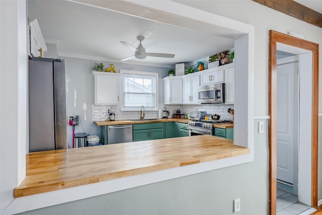 kitchen featuring tasteful backsplash, white cabinets, stainless steel appliances, wood counters, and a sink