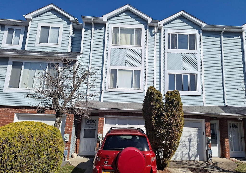 multi unit property featuring brick siding, an attached garage, and driveway