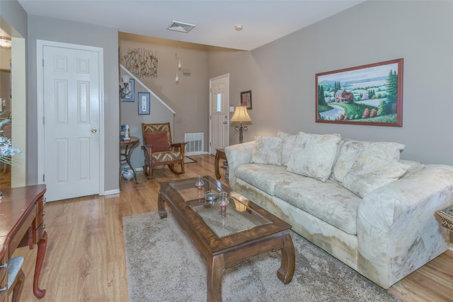 living room with stairway, baseboards, visible vents, and light wood-type flooring