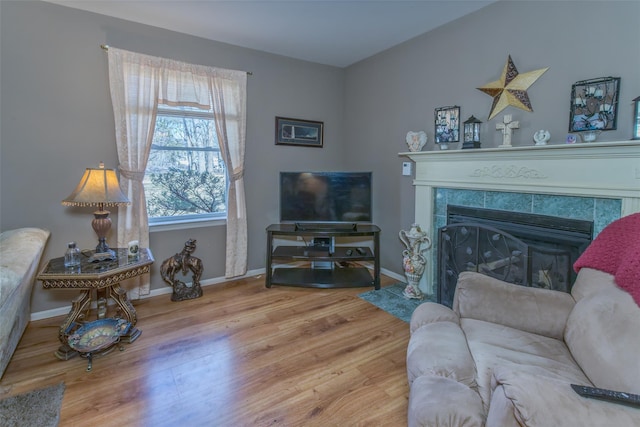 living area with a tiled fireplace, baseboards, and wood finished floors