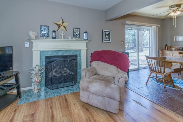 living area with a fireplace, wood finished floors, baseboards, and ceiling fan