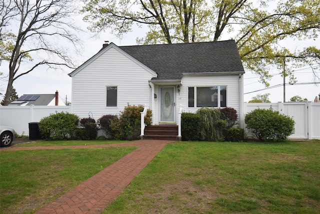view of front facade with fence, a chimney, a shingled roof, and a front lawn