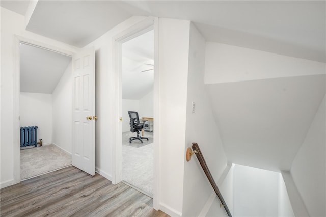 interior space with wood finished floors, lofted ceiling, radiator heating unit, carpet flooring, and an upstairs landing