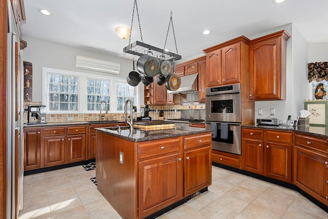 kitchen with a wall mounted AC, wall chimney range hood, backsplash, and stainless steel double oven