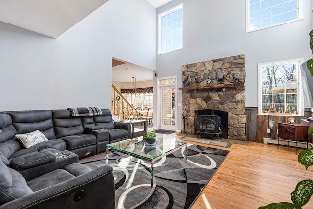 living room featuring stairway, a wood stove, wood finished floors, a notable chandelier, and a baseboard radiator