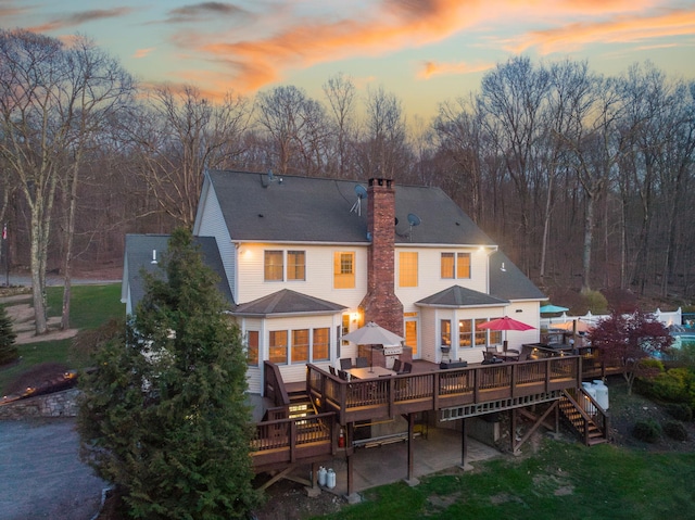 back of house at dusk with a deck and a chimney