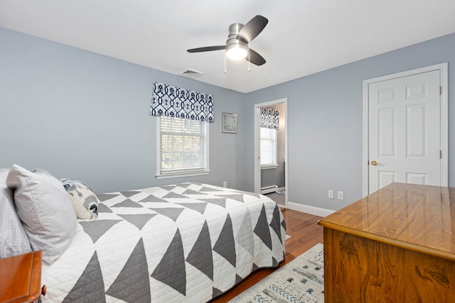 bedroom featuring visible vents, ceiling fan, baseboards, baseboard heating, and wood finished floors