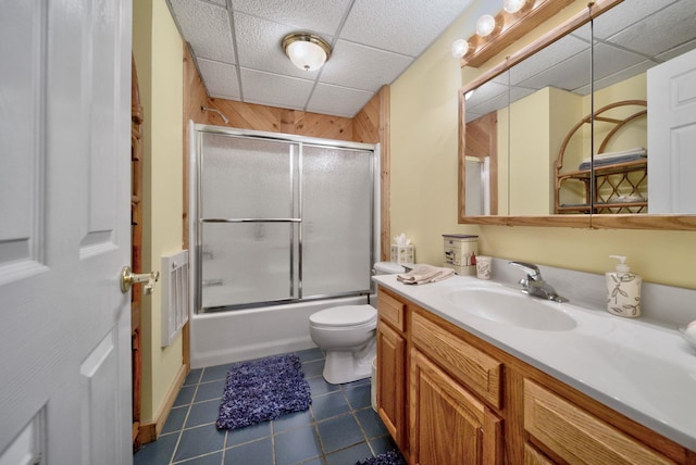 bathroom featuring toilet, a drop ceiling, tile patterned flooring, enclosed tub / shower combo, and vanity