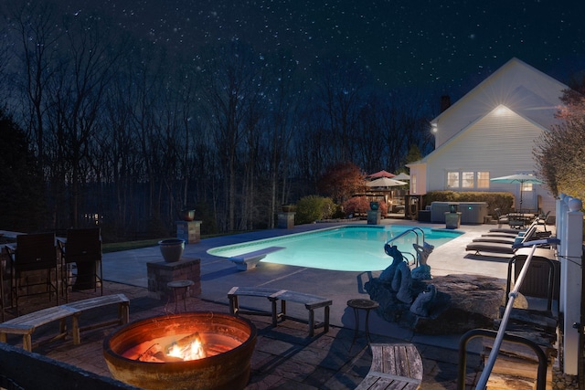 pool at twilight with a patio area, an outdoor pool, a fire pit, and a diving board