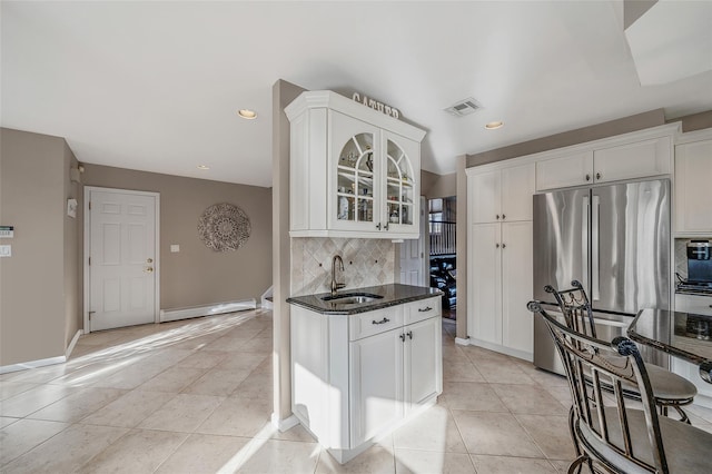 kitchen featuring light tile patterned floors, visible vents, dark stone counters, freestanding refrigerator, and a sink