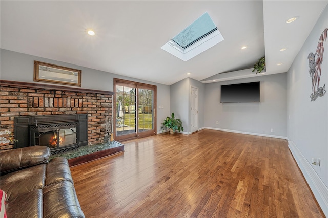 unfurnished living room featuring wood finished floors, recessed lighting, vaulted ceiling with skylight, a fireplace, and baseboards