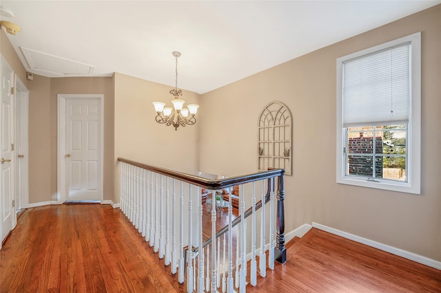 hall featuring baseboards, an upstairs landing, wood finished floors, and a chandelier