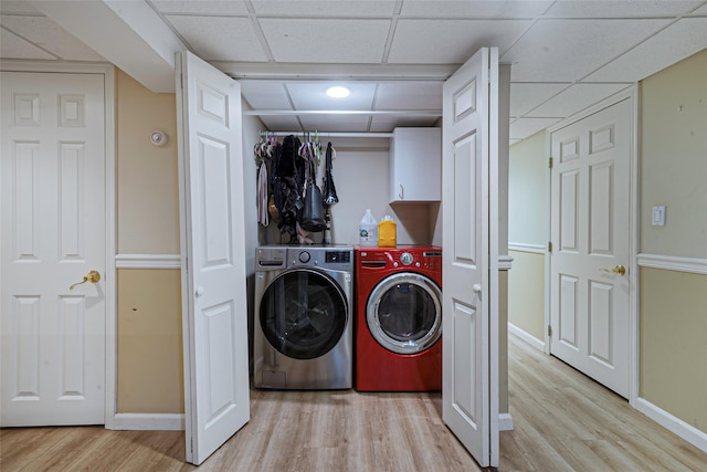 clothes washing area featuring cabinet space, washing machine and dryer, baseboards, and light wood-style floors