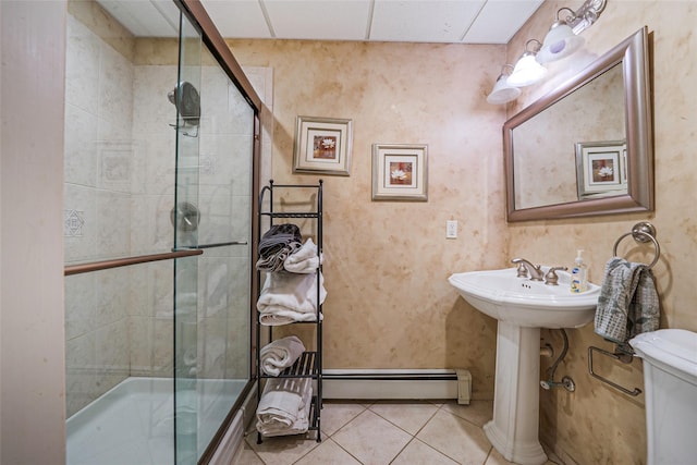 bathroom with tile patterned flooring, a baseboard heating unit, toilet, tiled shower, and a sink