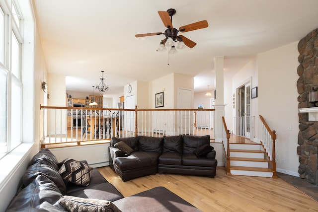 living area with ceiling fan with notable chandelier, plenty of natural light, wood finished floors, and a baseboard heating unit