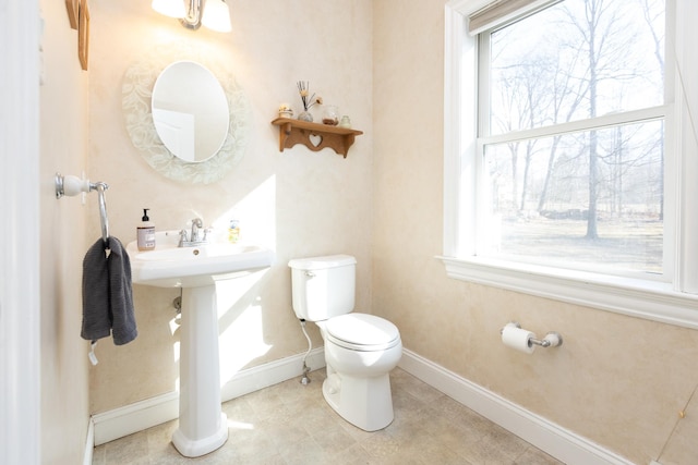 half bath featuring tile patterned flooring, toilet, a healthy amount of sunlight, and baseboards