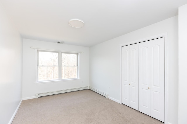 unfurnished bedroom featuring a baseboard heating unit, baseboards, visible vents, and carpet floors