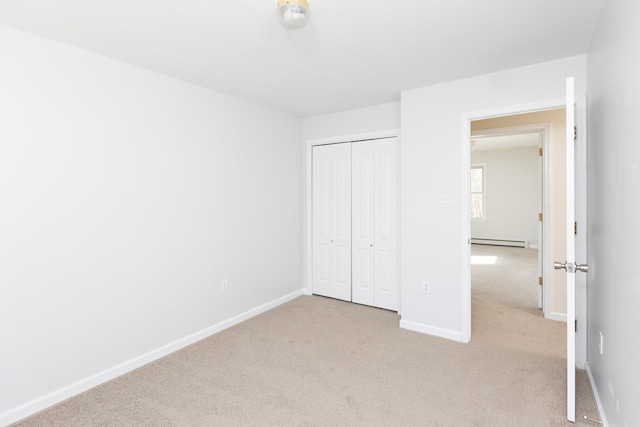 unfurnished bedroom featuring light colored carpet, baseboards, baseboard heating, and a closet