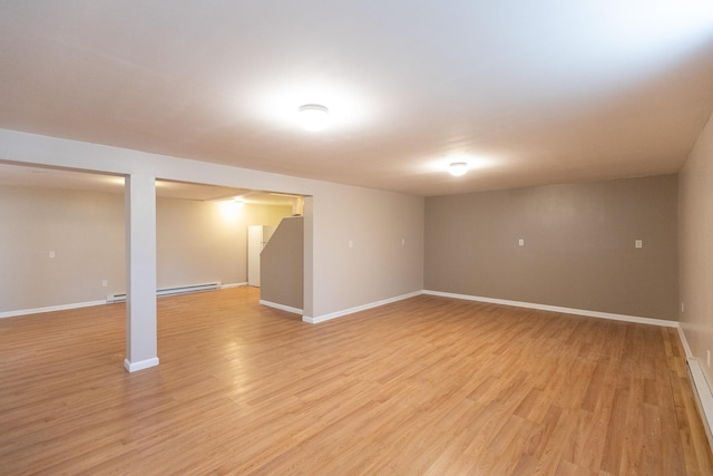 finished below grade area featuring light wood-style flooring, a baseboard heating unit, and baseboards