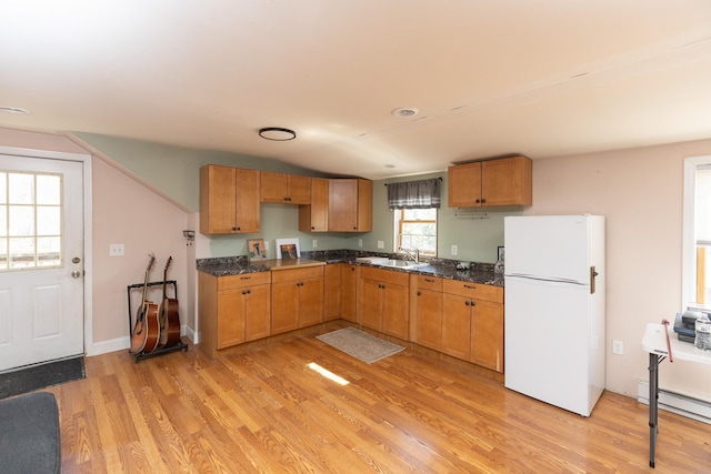 kitchen featuring a sink, dark stone countertops, light wood-style flooring, freestanding refrigerator, and a baseboard radiator