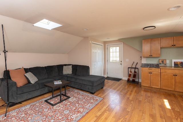 living room with baseboards, vaulted ceiling with skylight, and light wood-style flooring