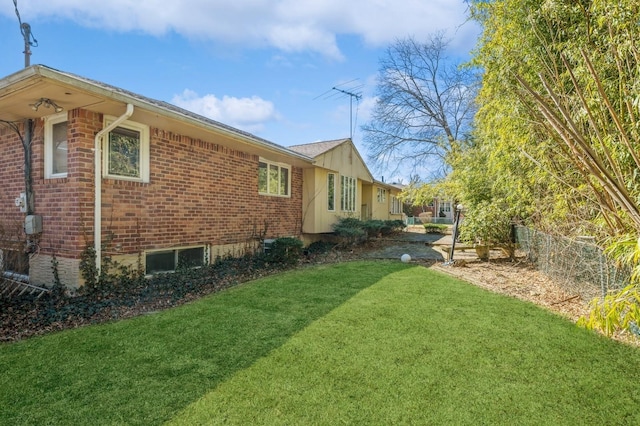 view of property exterior featuring brick siding, a lawn, and fence