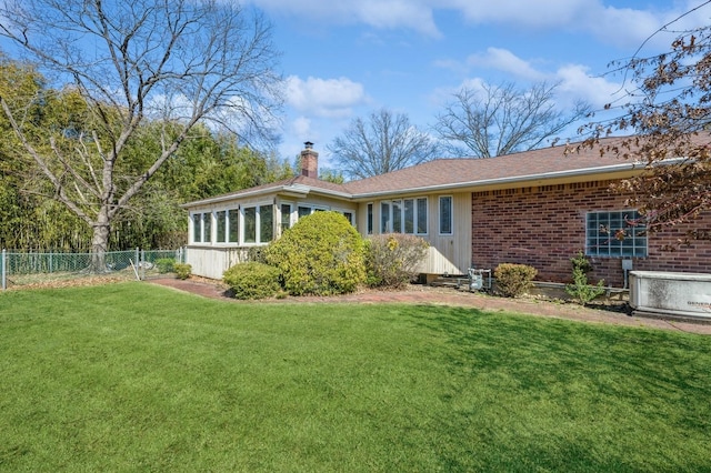 rear view of house featuring brick siding, a chimney, a yard, and fence