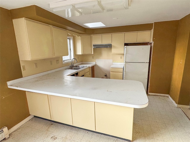 kitchen featuring a sink, freestanding refrigerator, a peninsula, light countertops, and light floors