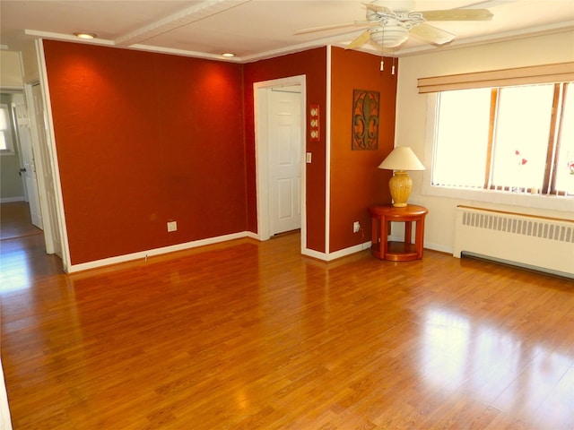 empty room featuring radiator heating unit, a ceiling fan, and wood finished floors