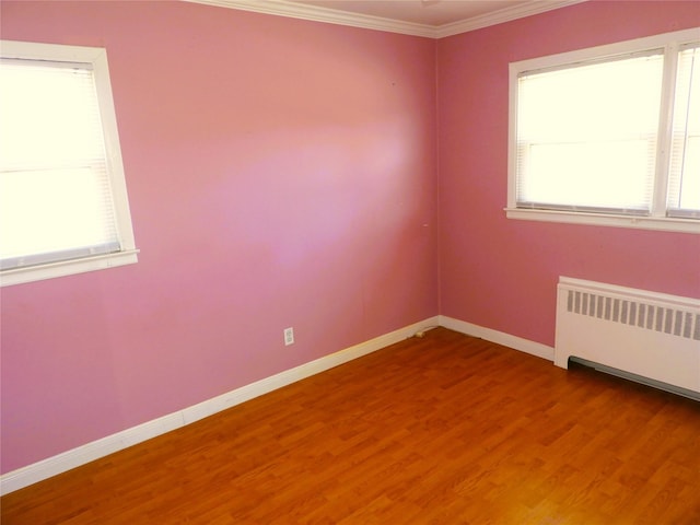 empty room featuring plenty of natural light, baseboards, radiator, and crown molding