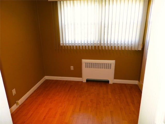 empty room with radiator, baseboards, and light wood finished floors