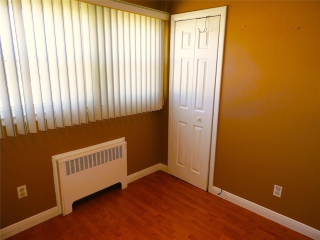 spare room featuring baseboards, radiator, and wood finished floors