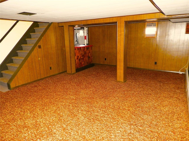 finished basement featuring carpet flooring, wood walls, stairs, and baseboards