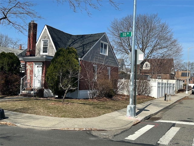 view of front of property with brick siding, a chimney, and fence