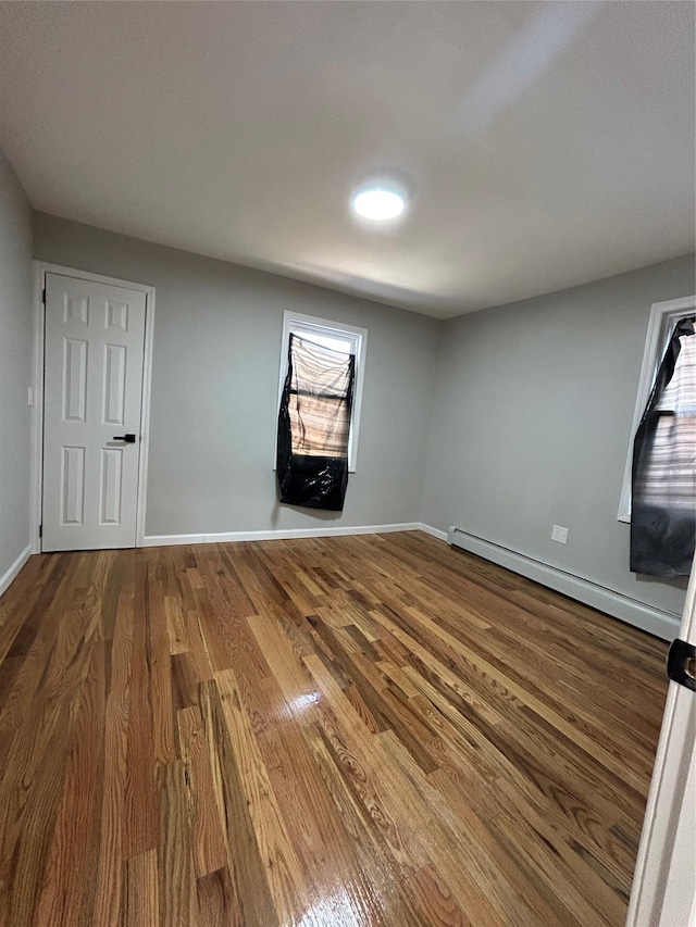 empty room with a baseboard radiator, baseboards, and wood finished floors