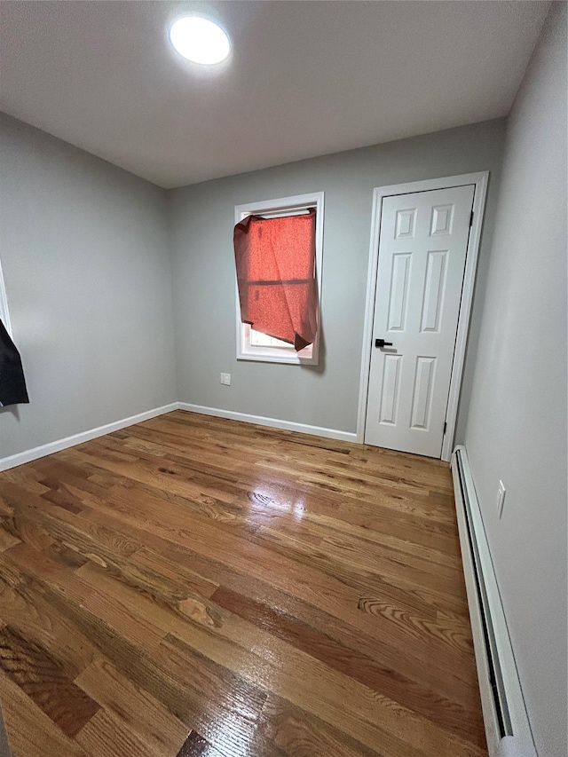 unfurnished bedroom featuring wood finished floors, baseboards, and baseboard heating