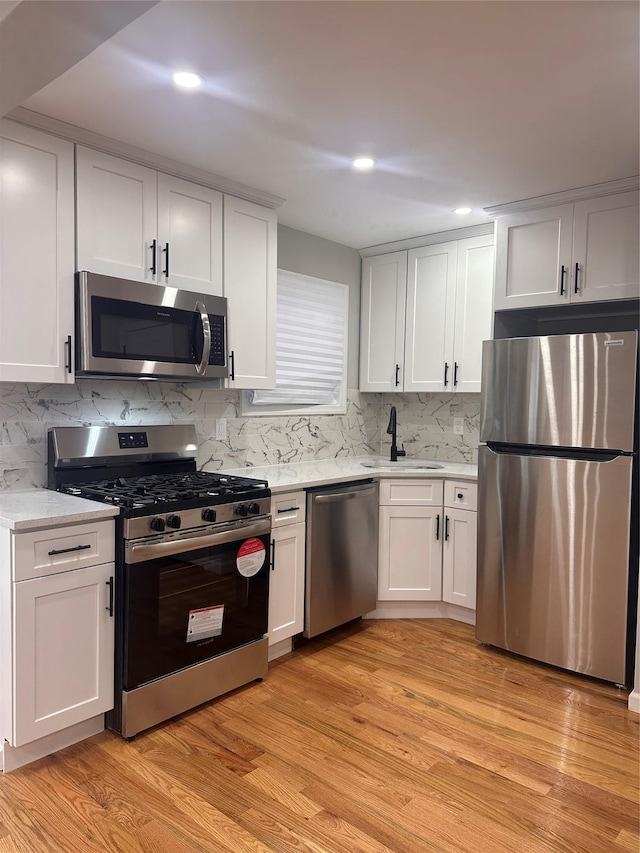 223-45 113th Dr, Queens Village, NY 11429 - kitchen with appliances with stainless steel finishes, light countertops, white cabinets, light wood finished floors, and decorative backsplash