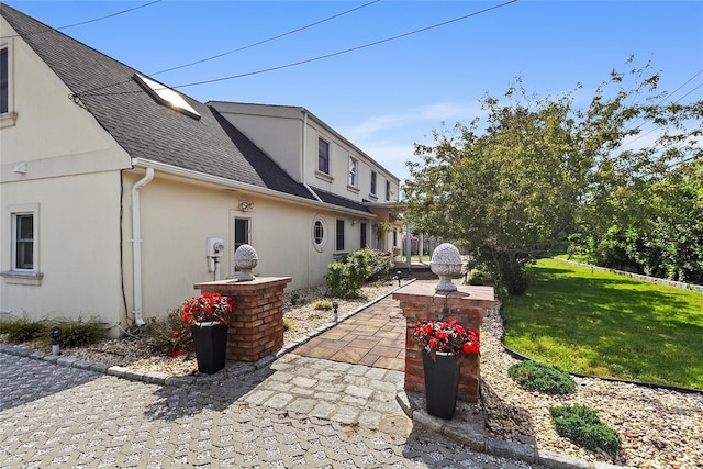 exterior space featuring stucco siding, a patio, a shingled roof, and a yard