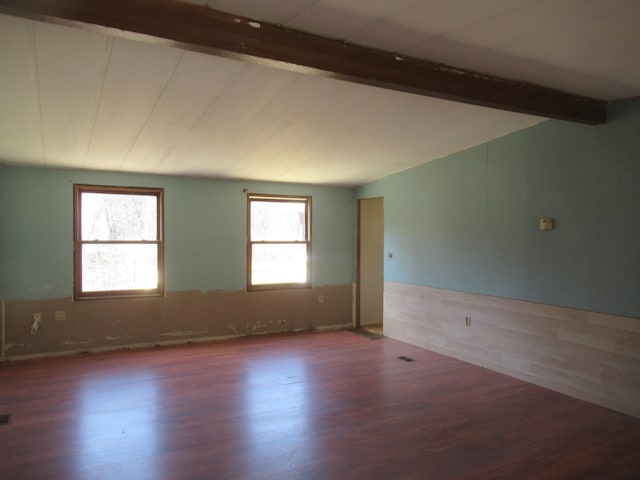 empty room featuring vaulted ceiling with beams, wood finished floors, and wainscoting