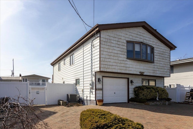 view of property exterior with fence, central AC, decorative driveway, a garage, and a gate