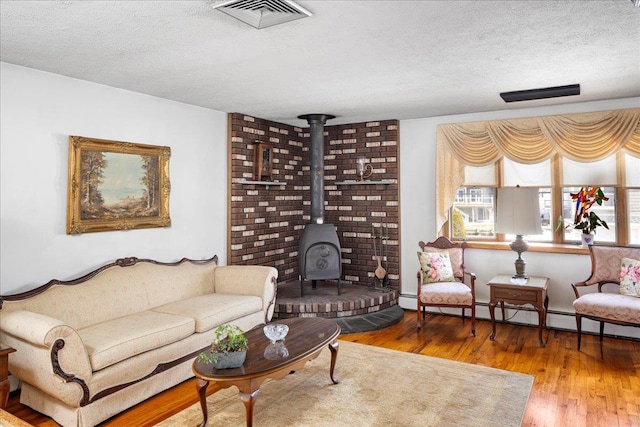 living area with visible vents, a baseboard heating unit, a textured ceiling, wood finished floors, and a wood stove