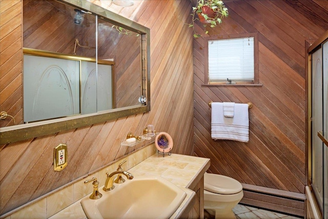 bathroom featuring a sink, toilet, a stall shower, and wood walls