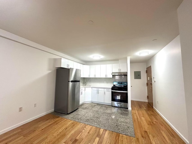 kitchen featuring light wood finished floors, electric panel, decorative backsplash, under cabinet range hood, and appliances with stainless steel finishes